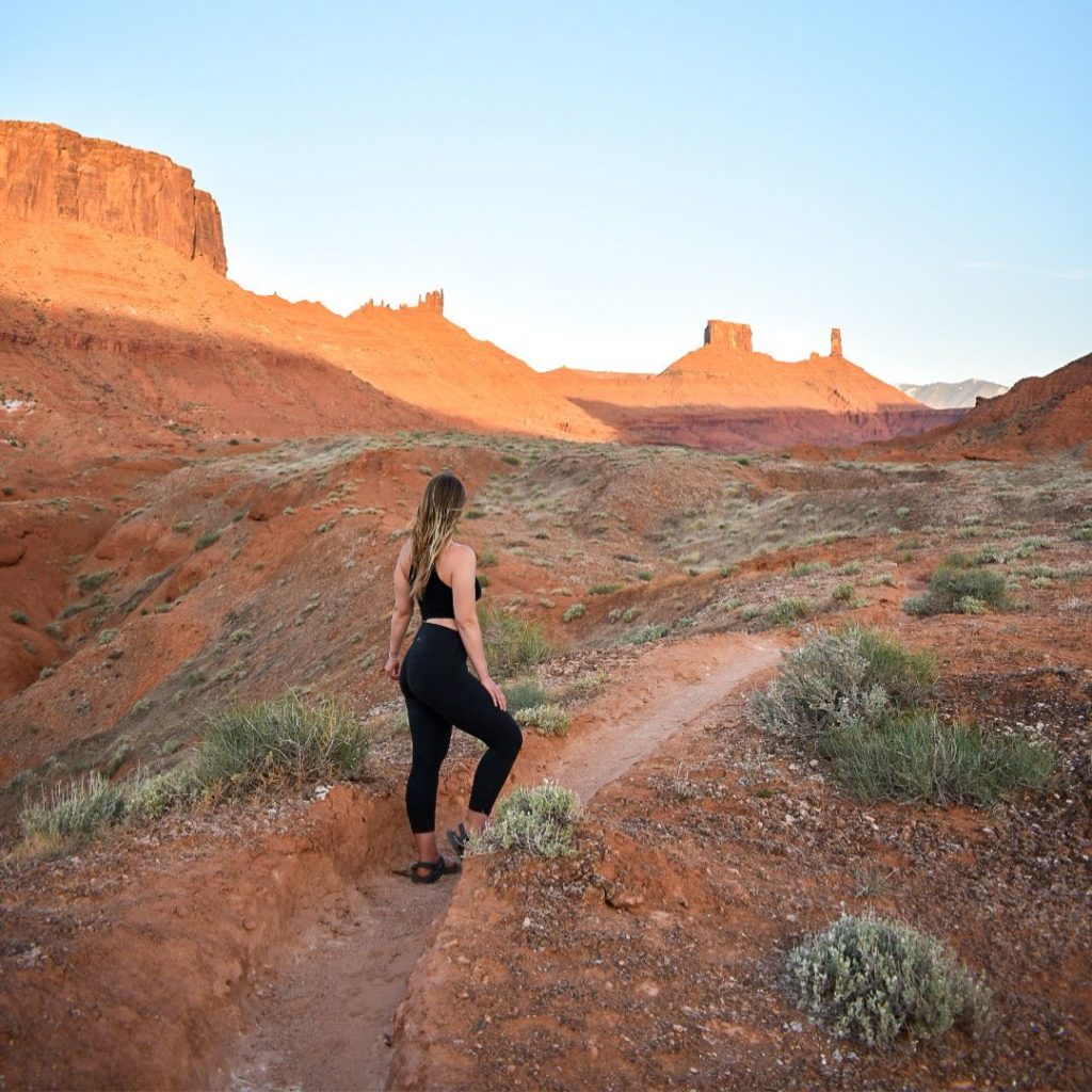 Woman stands facing Castleton Tower in Moab at sunset.