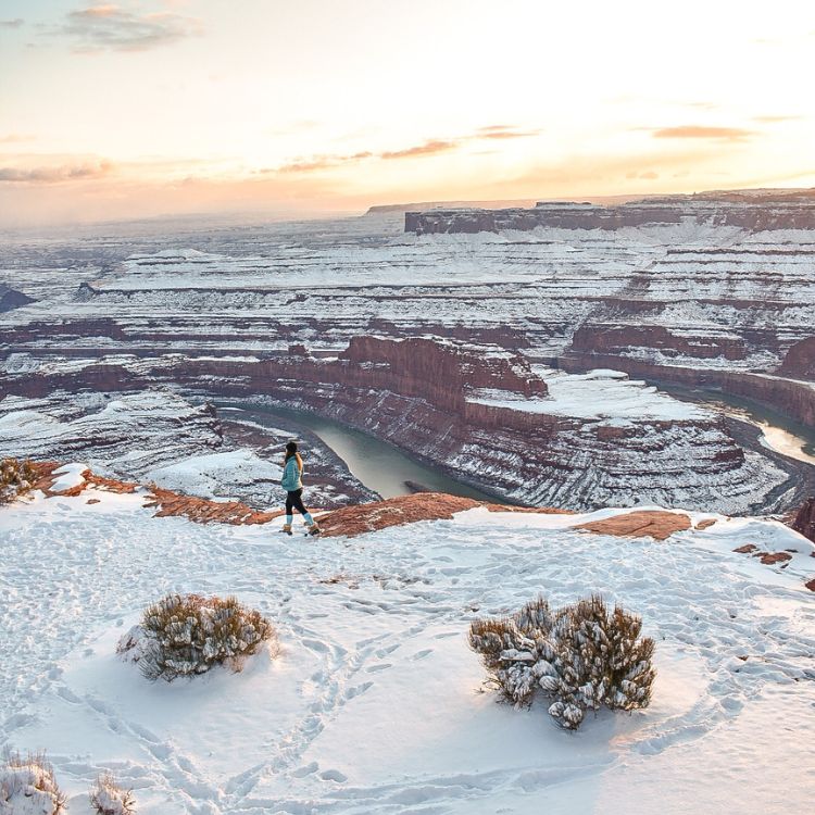 Woman hikes through the snow at Dead Horse Point State Park at sunset.