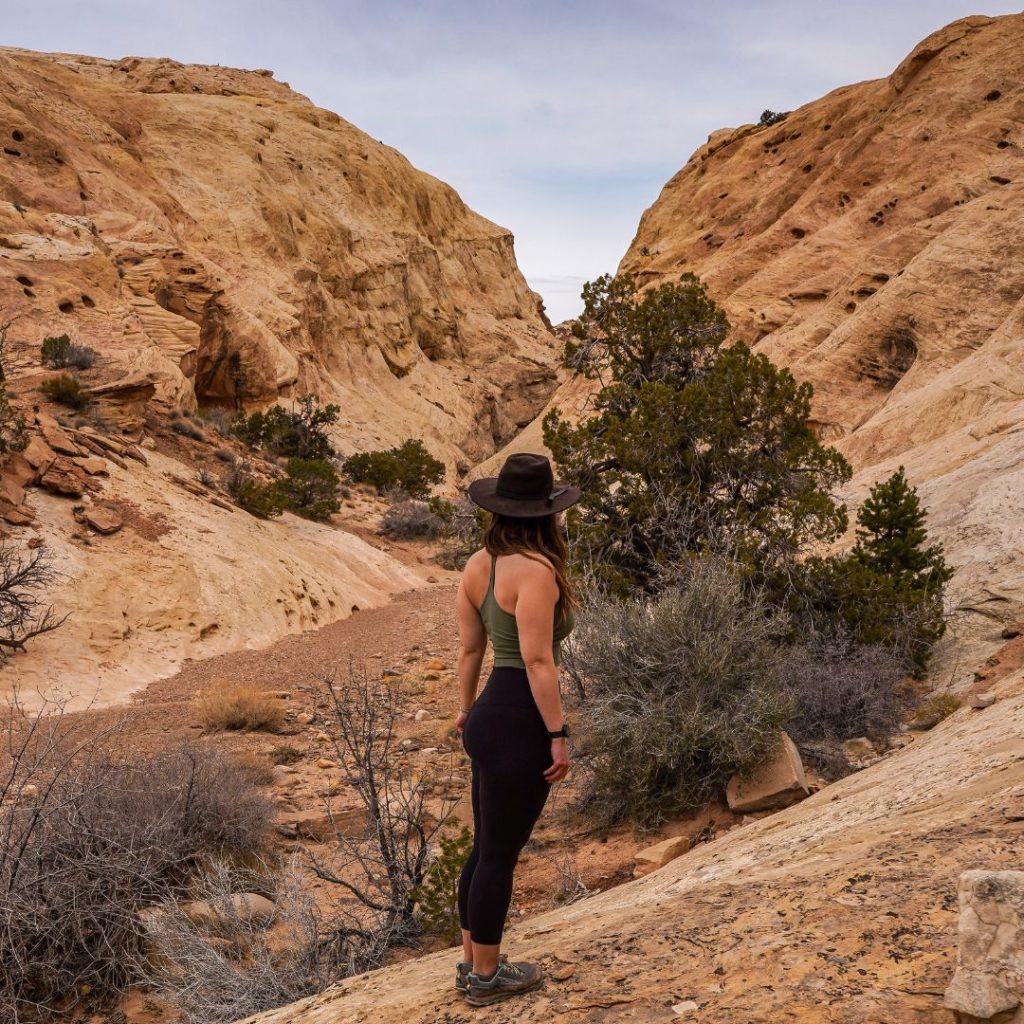 Woman wearing leggings and a black hat hiking in the desert.