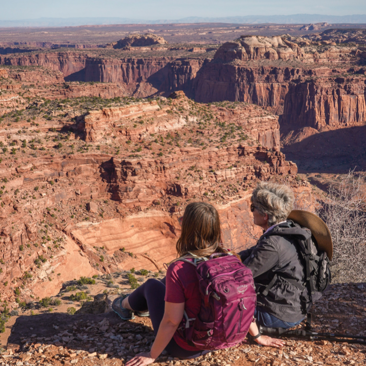 Mother and daughter sit on the edge of a cliff in Canyonlands National Park.