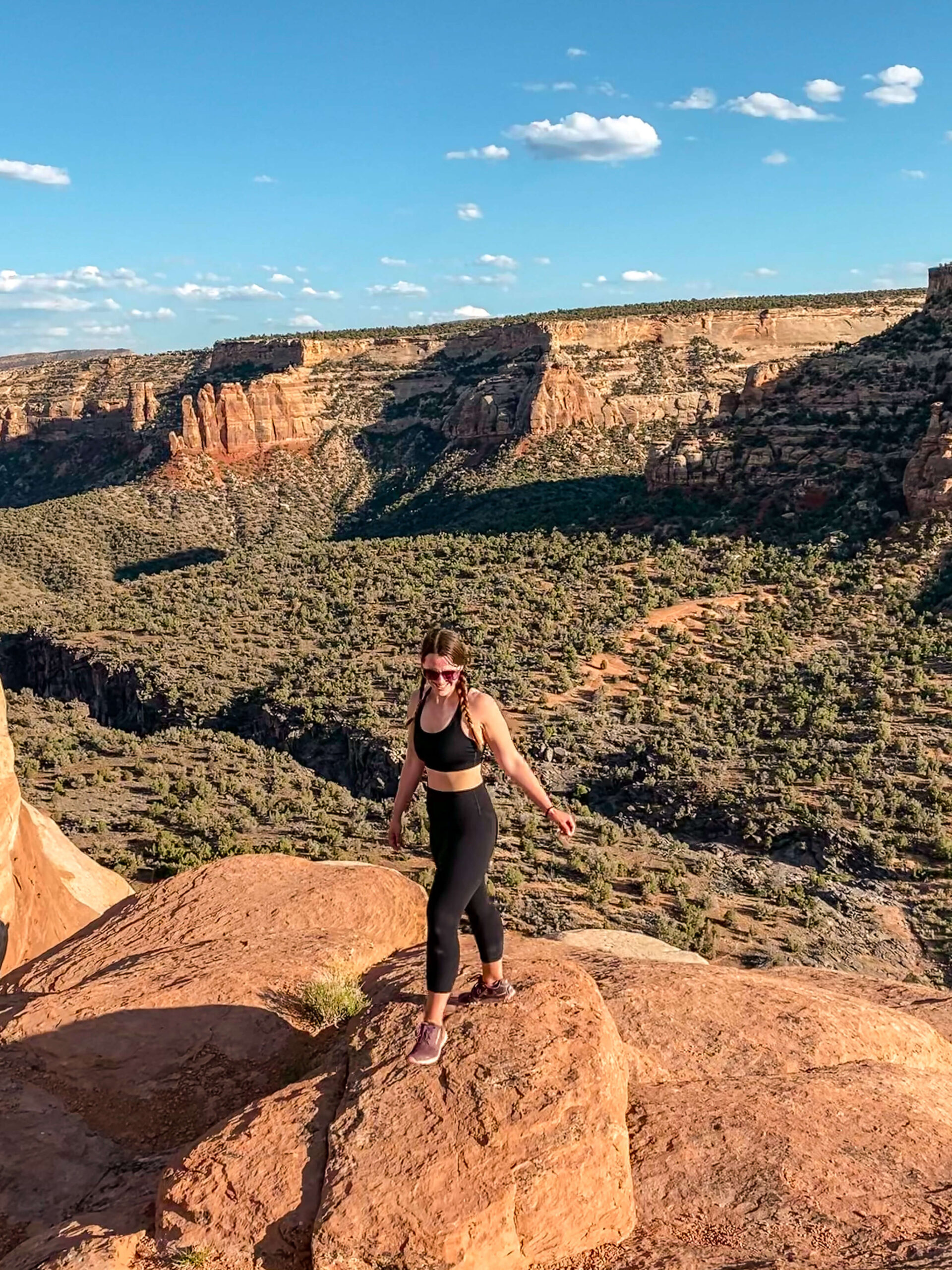 Woman wearing a black sports bra and leggings stands on a sandstone rock overlooking Ute Canyon in Colorado National Monument.