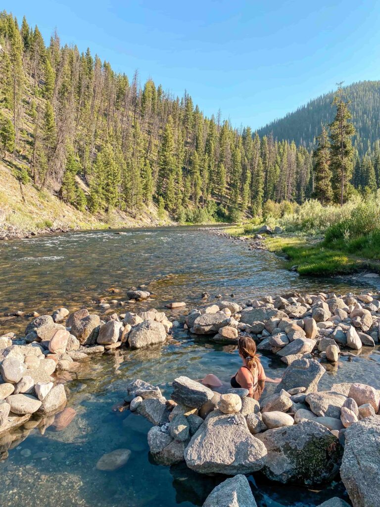 Woman sits in a hot springs next to a river in Idaho surrounded by rocks.