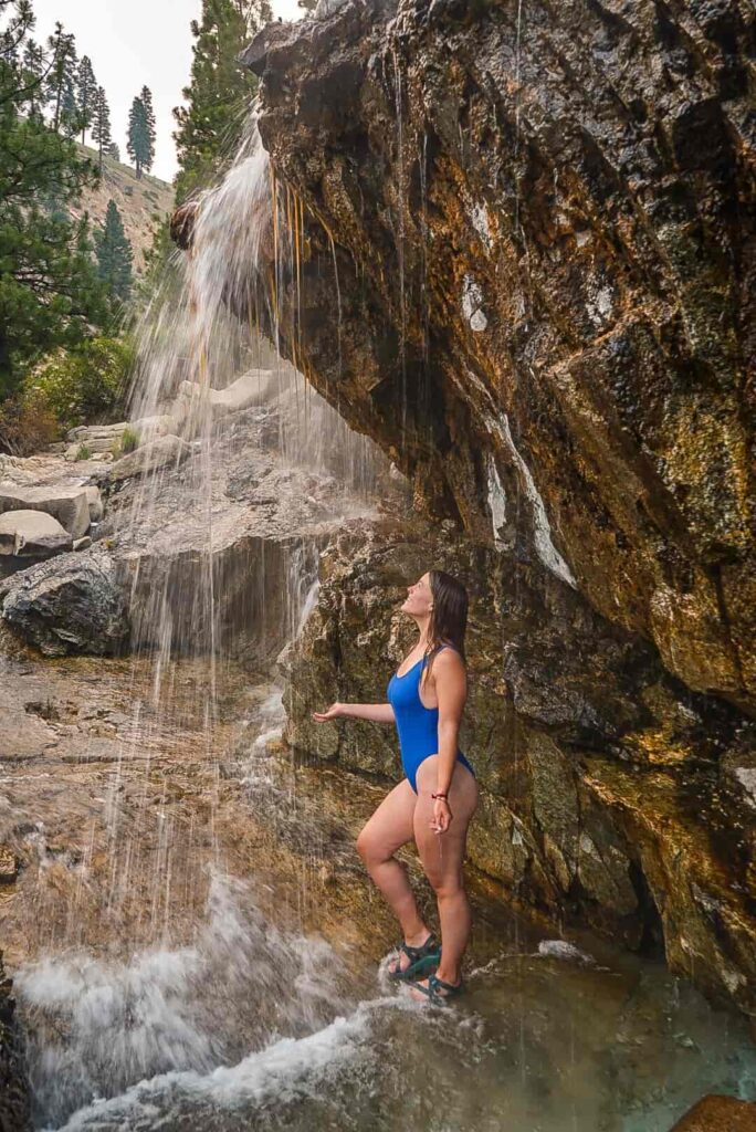 Woman wearing a blue bathing suit stands under a hot springs waterfall in Idaho.