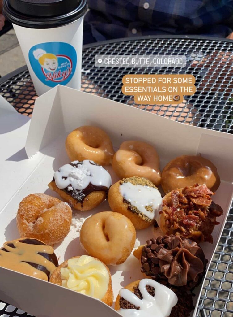 Box of 12 mini donuts with various toppings including chocolate peanut butter, s'mores, and maple bacon with a cup of coffee with a Nicky's logo.