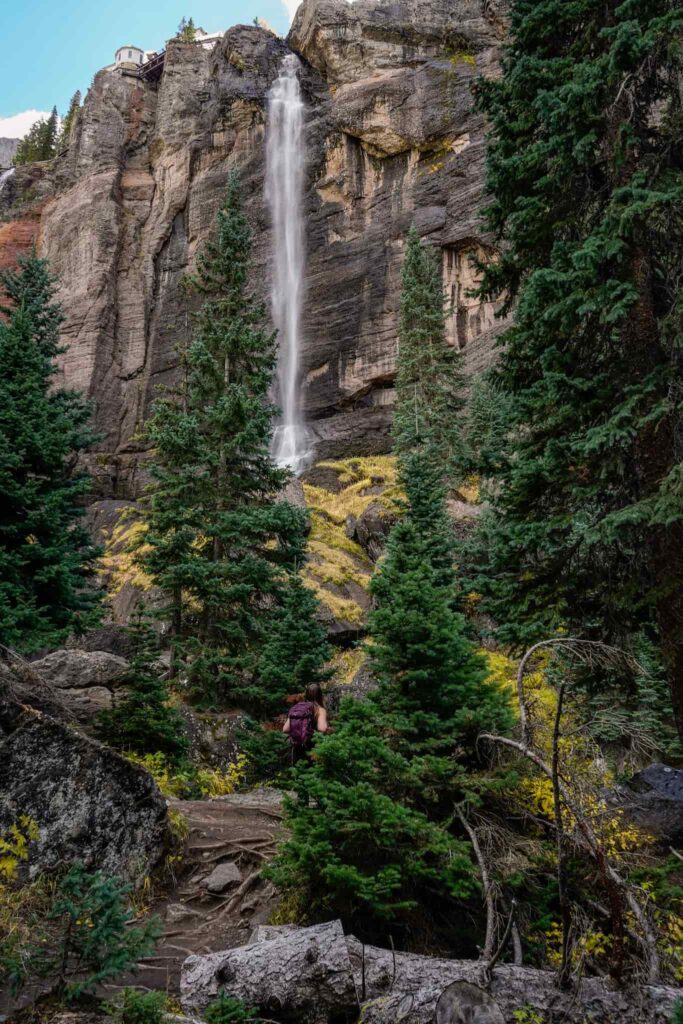 Woman standing below Bridal Veil Falls while hiking in Telluride in the fall.