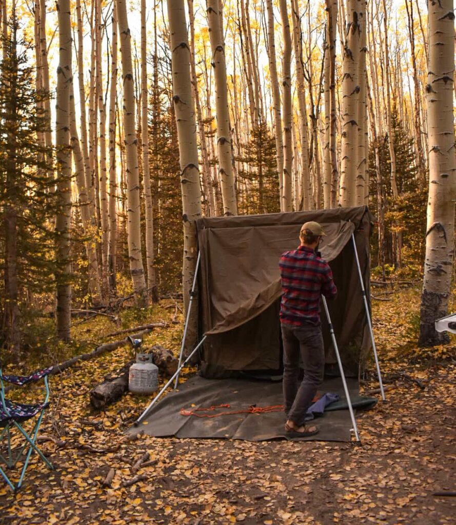 A man setting up a safari tent in a forest of golden aspen trees while camping in Telluride in the fall.