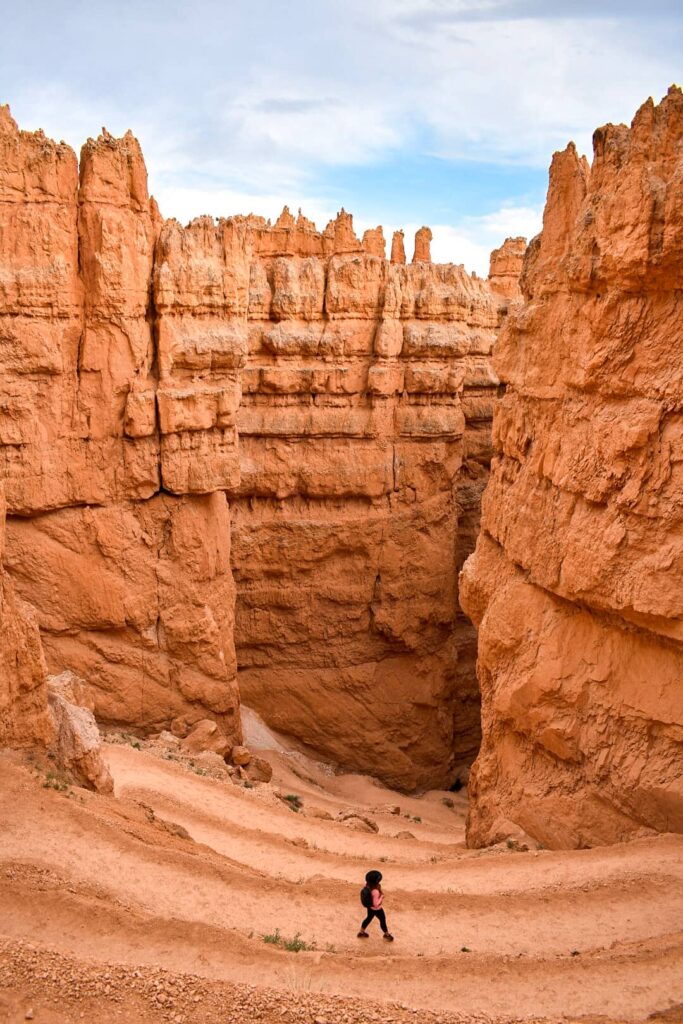 A woman stands on a winding trail in an orange sandstone canyon while hiking in Bryce Canyon National Park.