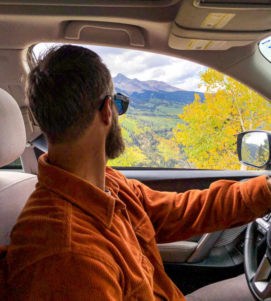 Man in orange shirt drives in the mountains during the fall.