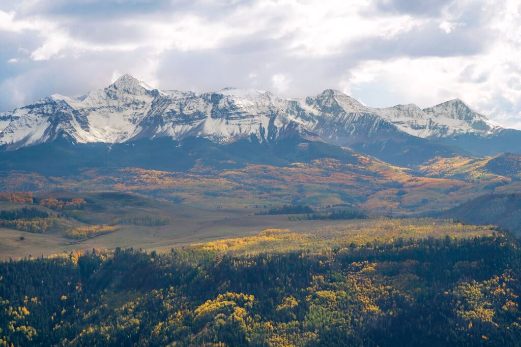 Snow covered mountain peaks with large forests of golden aspen trees and meadows in Telluride in the fall.