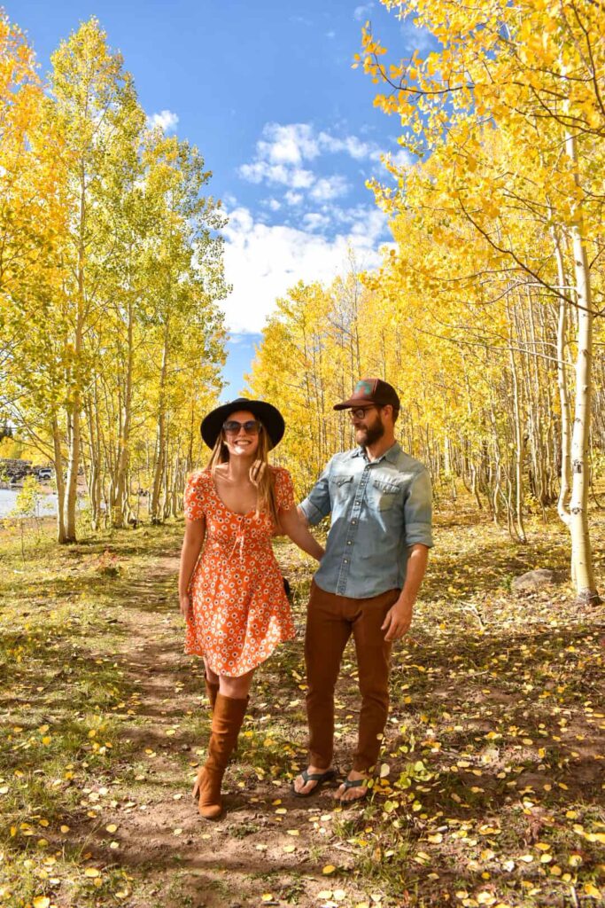 A smiling couple walks through a grove of golden aspen trees during the fall.