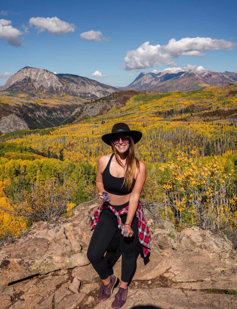 Woman on a fall hike in Crested Butte with golden aspens and mountains behind her.