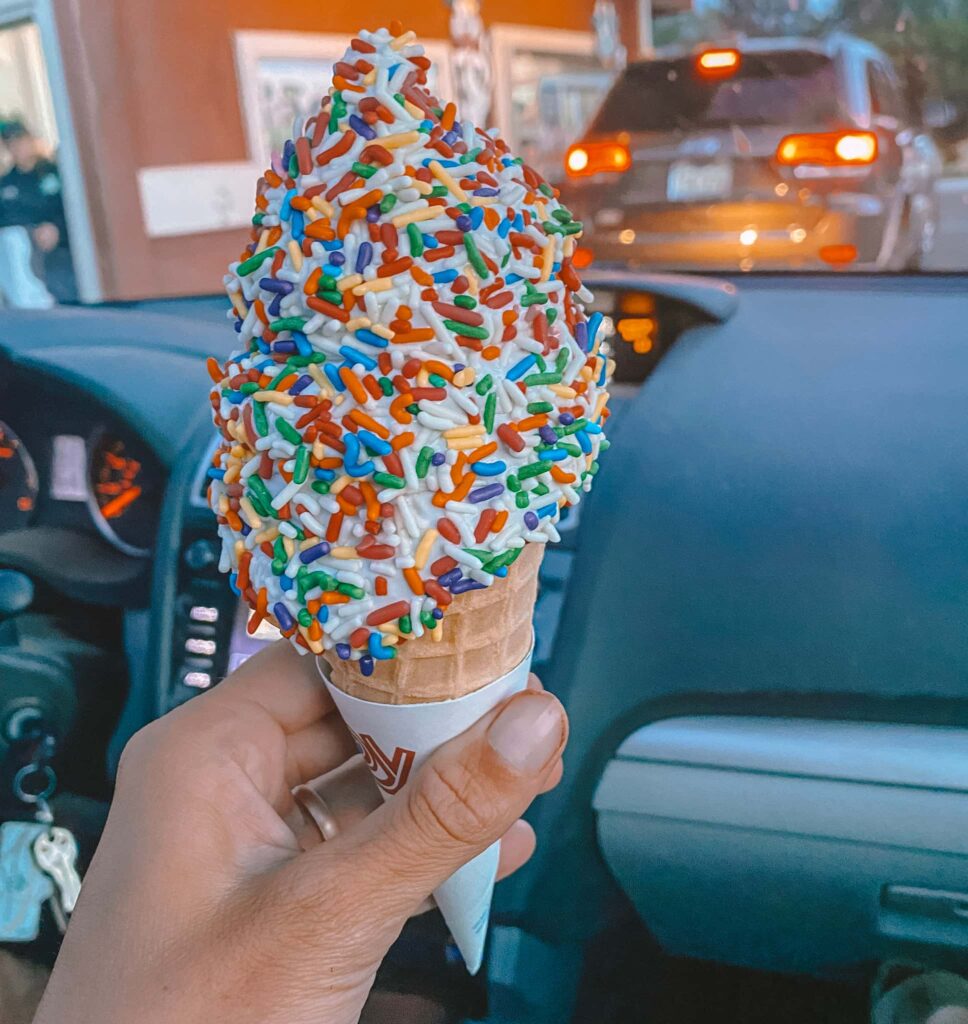 Vanilla soft serve ice cream with rainbow sprinkles in a cone.