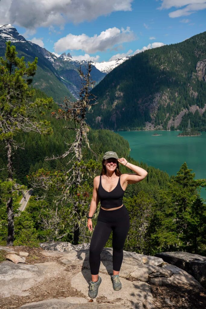 Woman stands in an all black hiking outfit on top of Thunder Knob above Diablo Lake in the North Cascades.