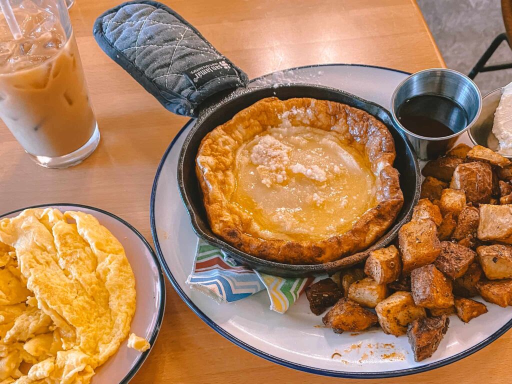 An iced coffe, Dutch baby pancakes with potatoes, and a side of scrambled eggs.