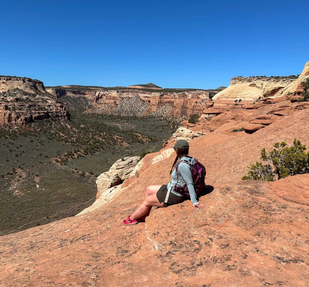 Woman sitting on a sandstone rock formation overlooking a verdant canyon while wearing hot pink Altra Lone Peak trail runners.