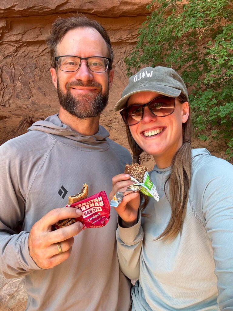 A couple eating granola bars on a hike.