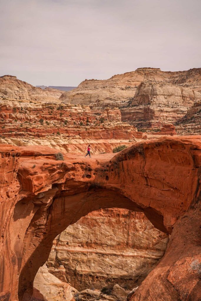 Woman hikes across an arch in Capitol Reef National Park.