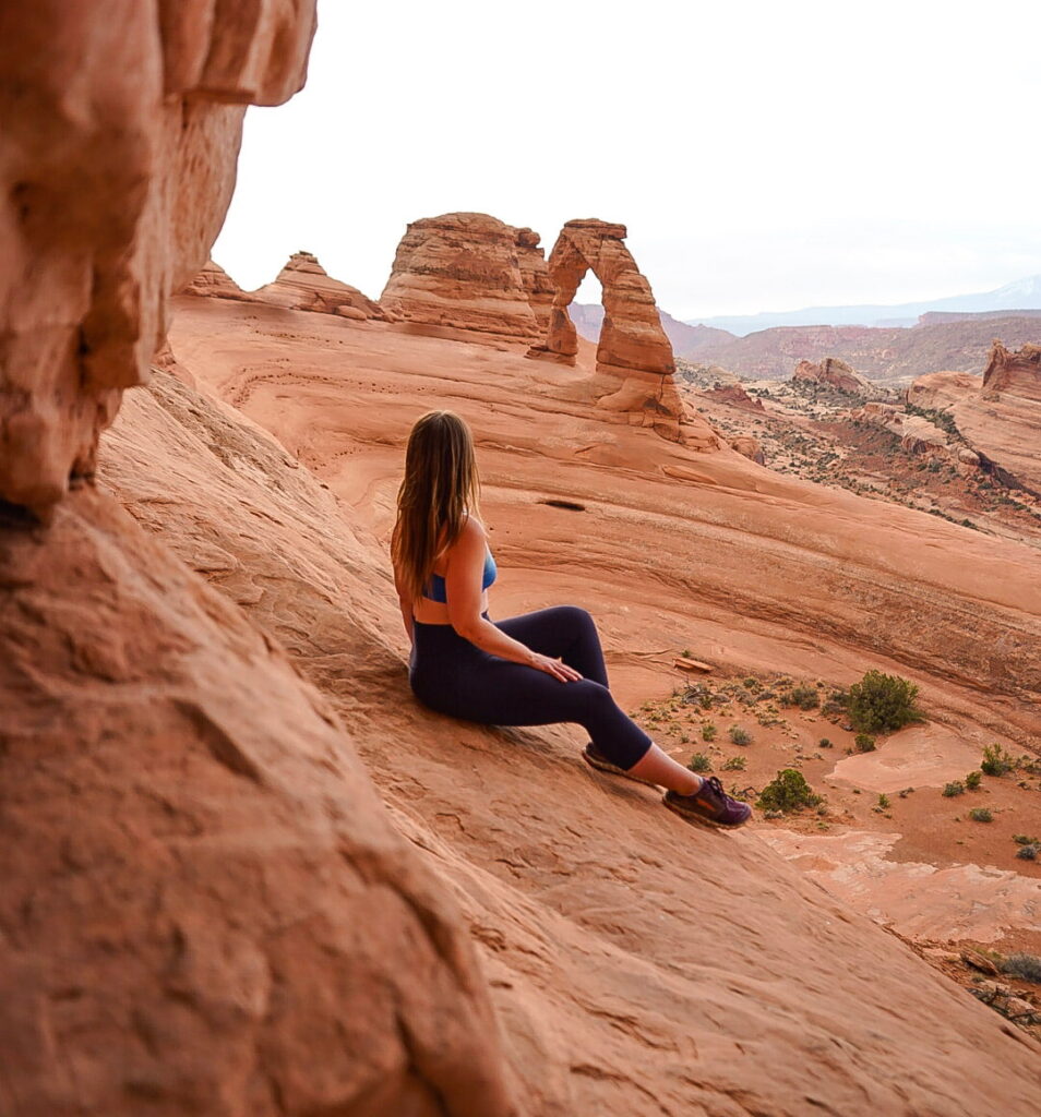 Woman sitting on rock with Delicate Arch in the distance.