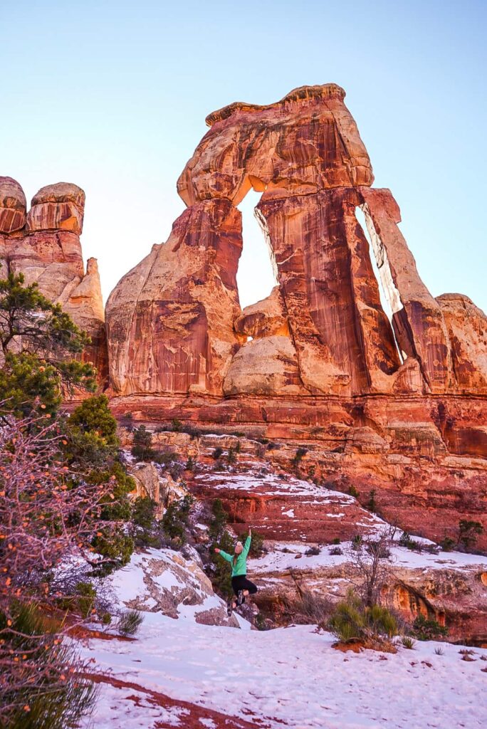 Woman jumping in front of Druid Arch in the Needles District of Canyonlands National Park while on a hike in Southern Utah.