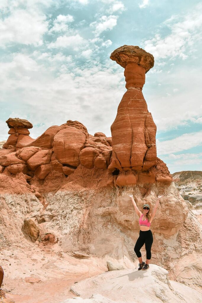 Woman with her arms up in front of the Toadstool Hoodoos.