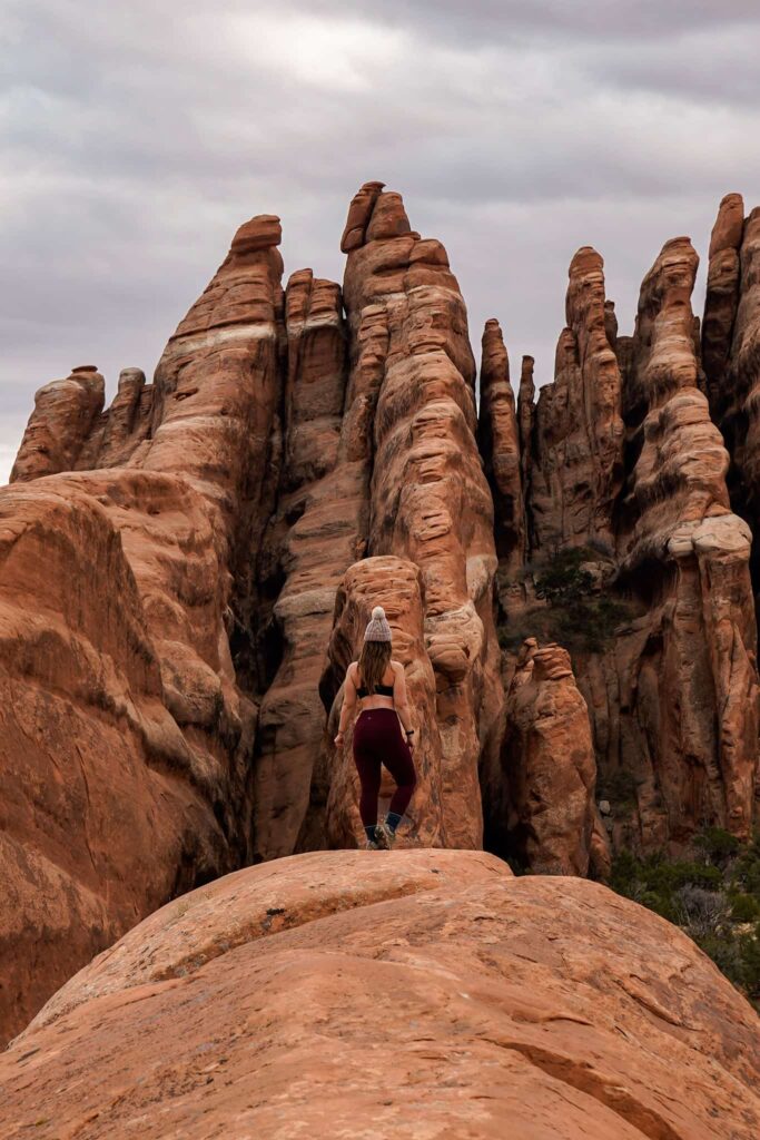 Woman standing on slickrock with sandstone rock fins in front of her in Arches National Park.