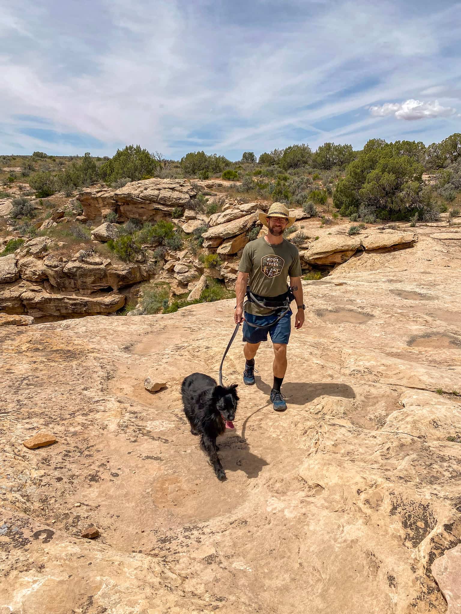 Man hiking with a black dog on a hands-free Ruffwear leash.