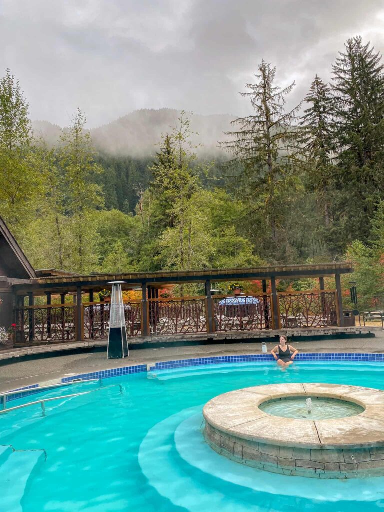 Woman soaking in a hot spring pool in Olympic National Park surrounded by foggy trees.