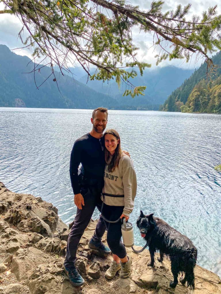 A couple and black dog stand in front of Lake Crescent on their honeymoon in Olympic National Park.