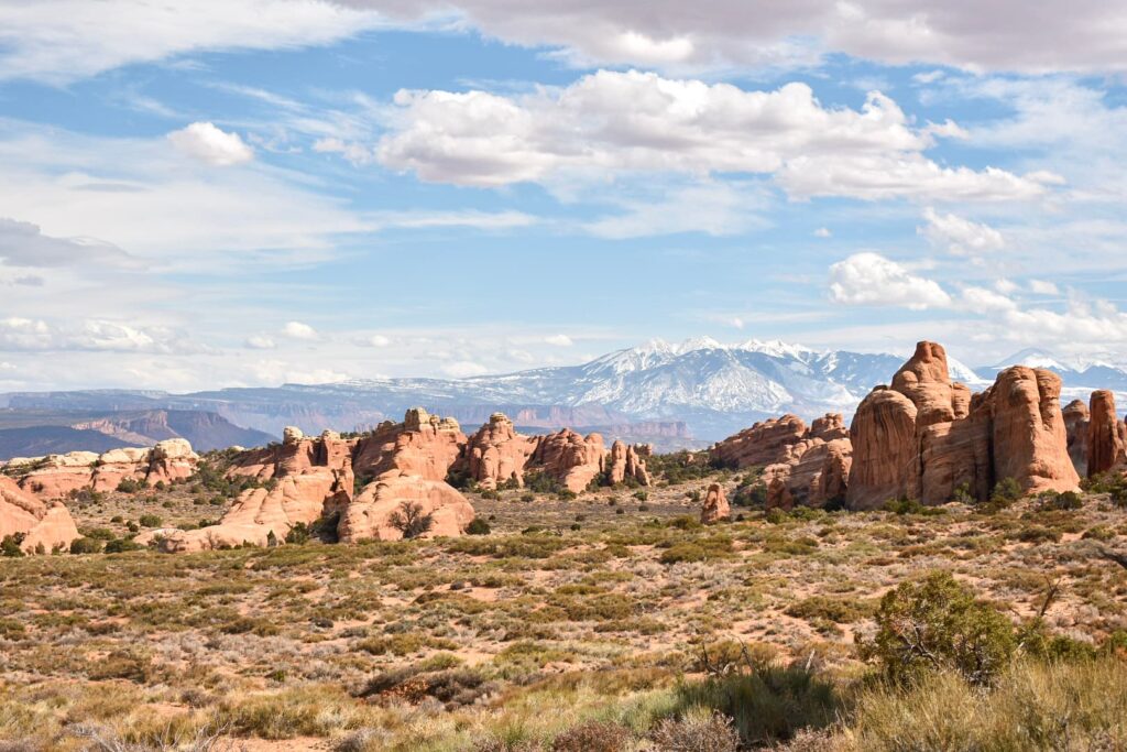 A view of orange sandstone rock formations with snow-capped mountains in the background.