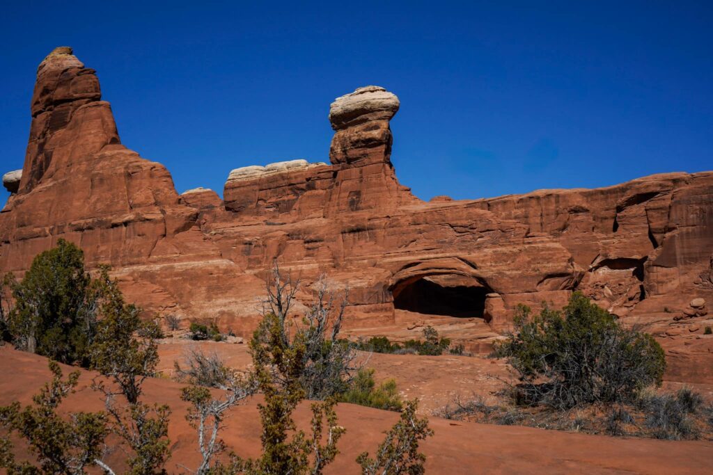 A sandstone wall in the desert with a thick arch in the middle and a bright blue sky.
