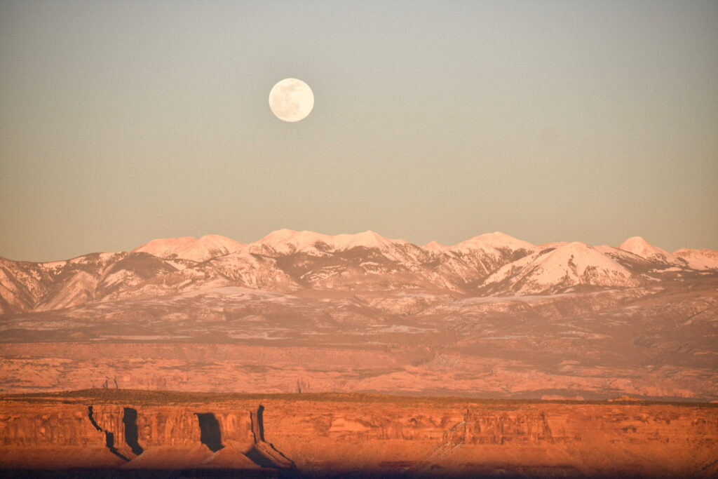 Full moon rising over the La Sal mountains with the red rock canyons of Moab, Utah, in the foregound.