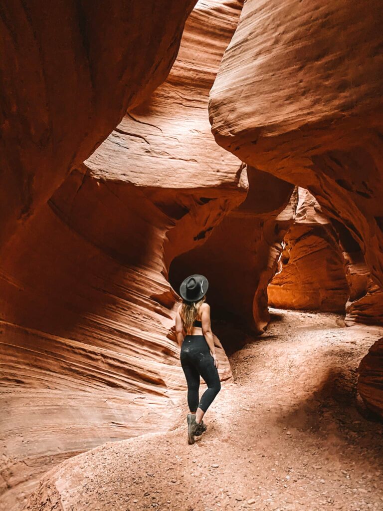 A woman in a black hat stands in a slot canyon in southern Utah near Hanksville.