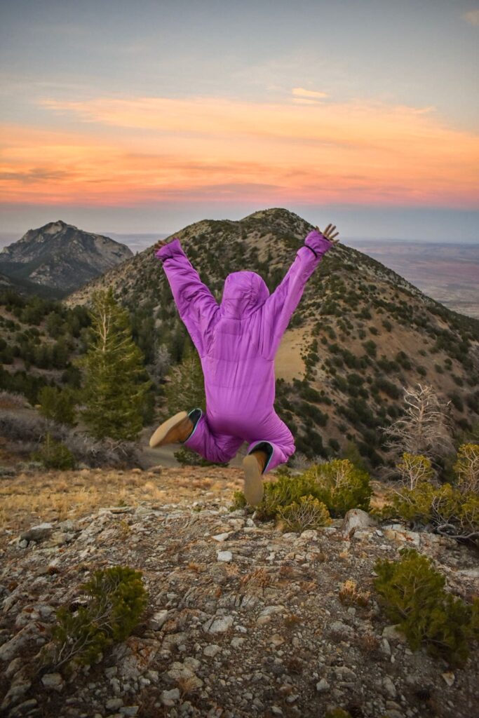 woman jumping in a purple sleeping bag suit in the mountains at sunset
