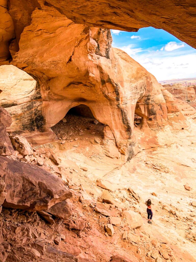 Woman stands at the bottom of a large alcove with 5 unique arches near Hanksville, Utah.
