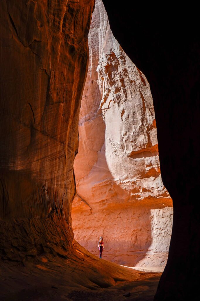 Woman stands at the mouth of an orange slot canyon.