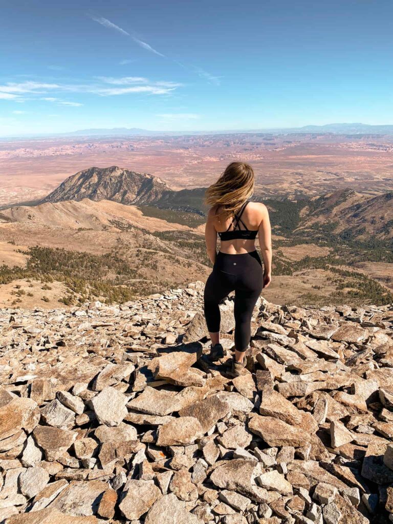 Woman stands on the summit of a mountain she climber overlooking the desert around Hanksville, Utah.