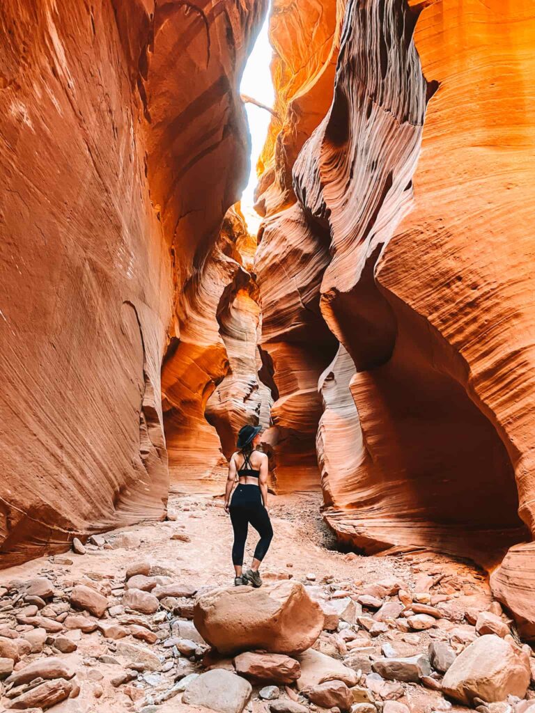 Woman stands on a rock in a tall sandstone slot canyon in southern Utah near Hanksville.