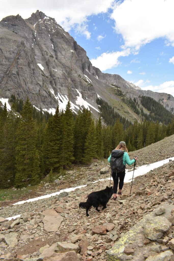 Woman hiking on a rocky trail with a black dog behind her in the mountains in Colorado.