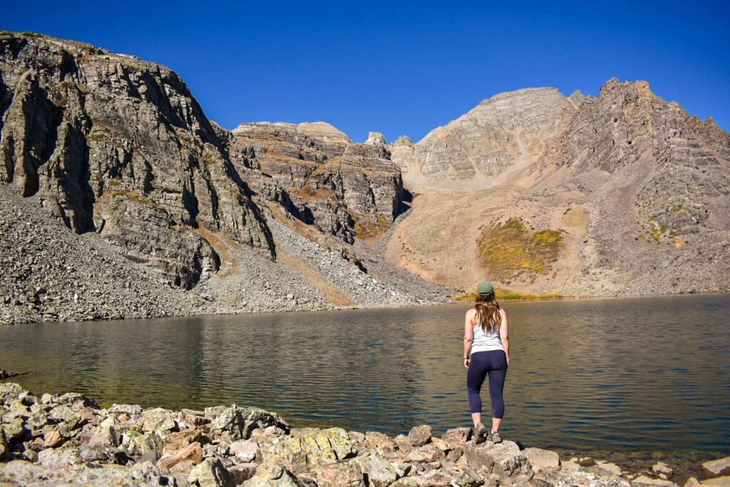 Woman standing on the shore of an alpine lake in front of mountains.