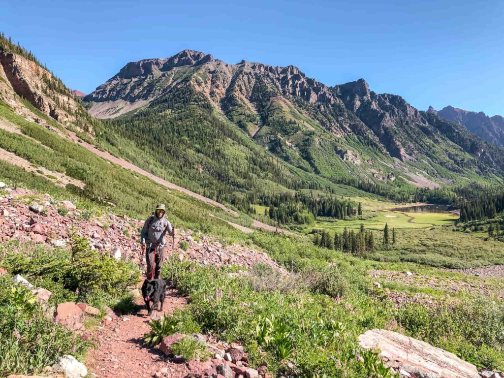 A man with a black dog tied to his waist hikes on a red trail in the mountains outside of Aspen, Colorado.
