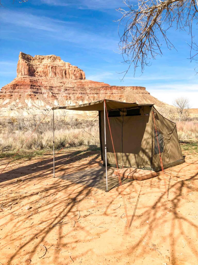 A safari style tent and dog bed in front of a desert butte.