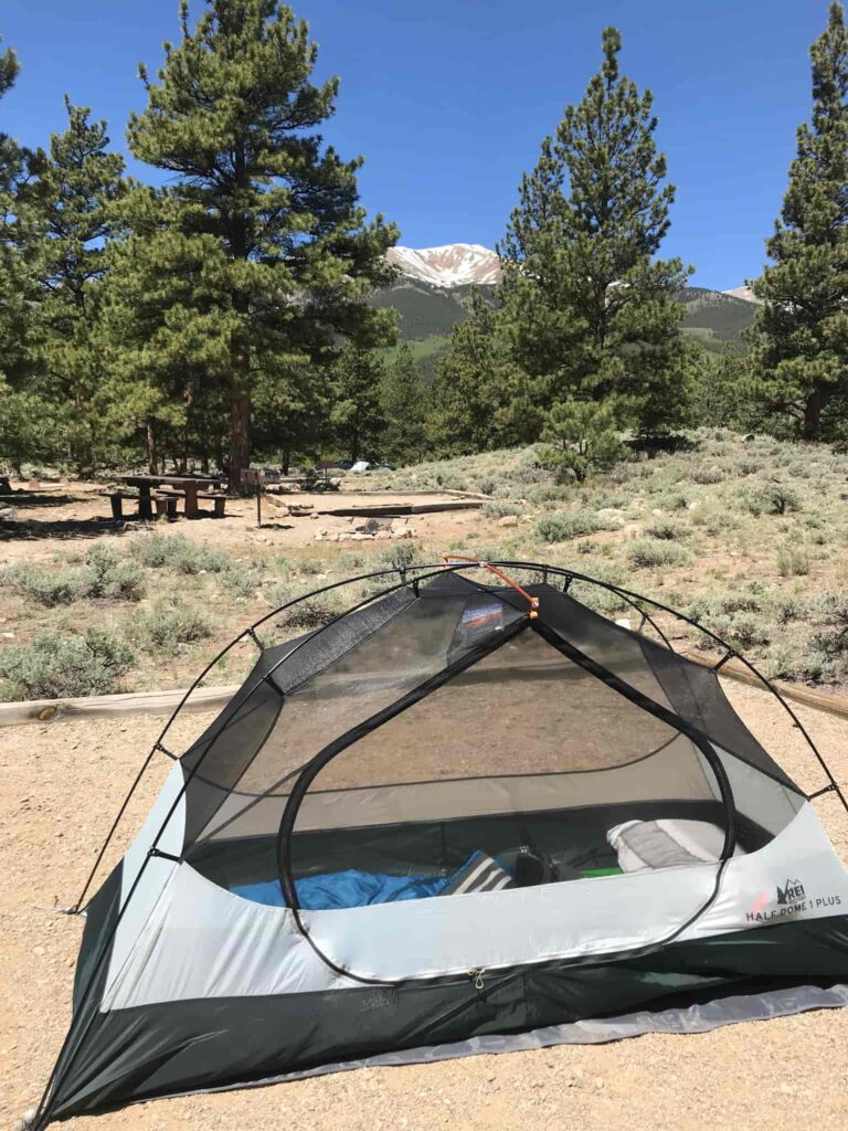 A tent in an otherwise empty campground with a snow-covered mountain in the background.