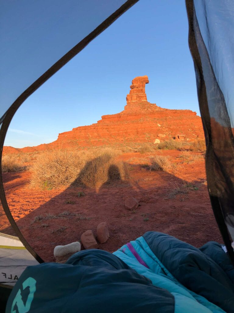 Looking out of an open tent at a red rock formation while camping in Valley of the Gods in Utah.